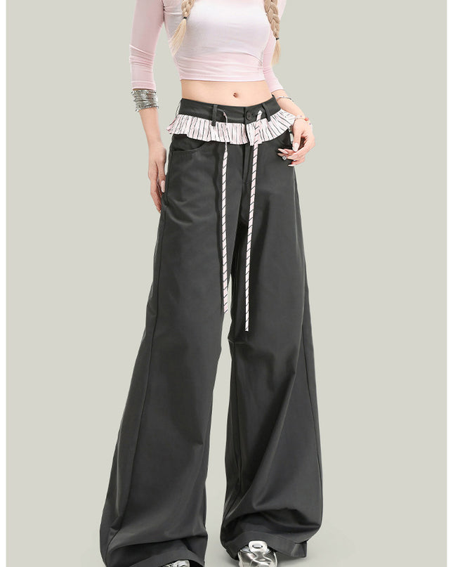 Person wearing a pink top and black wide-leg pants with a white belt on a light gray background