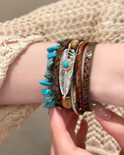 Close-up of a wrist wearing multiple bracelets with turquoise stones and feather designs.
