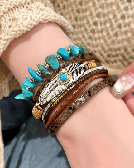 Close-up of a wrist wearing multiple bracelets with turquoise stones and feather designs.