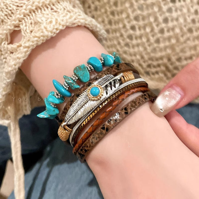 Close-up of a wrist wearing multiple bracelets with turquoise stones and feather designs.