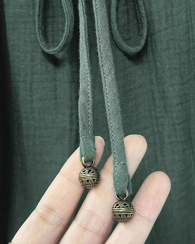 Hand holding a green fabric strap with decorative metal ends against a dark background