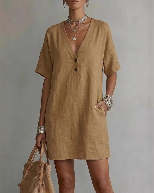 Woman wearing a brown dress holding a beige bag against a gray background