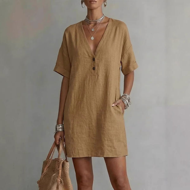 Woman wearing a brown dress holding a beige bag against a gray background