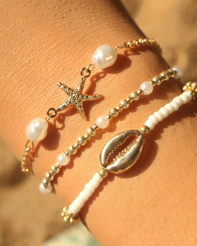 Three beaded bracelets with starfish and shell charms on a wrist against a blurred natural background.