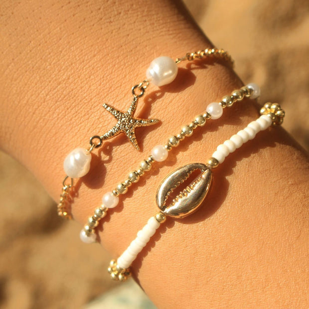Three beaded bracelets with starfish and shell charms on a wrist against a blurred natural background.