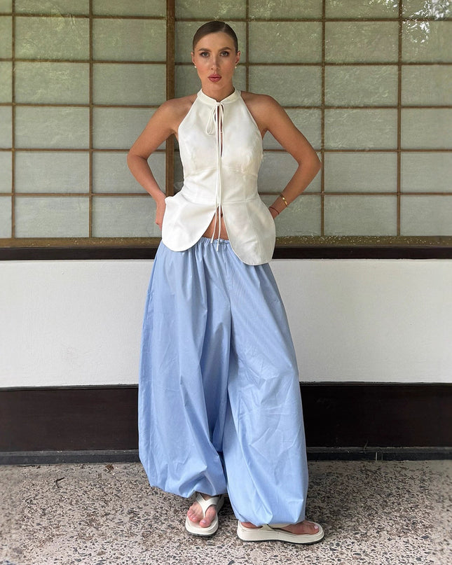 Woman wearing a white sleeveless top and light blue wide-leg pants standing against a tiled wall.