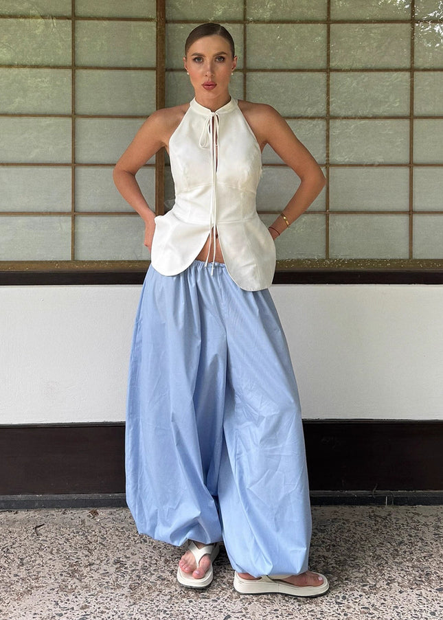 Woman wearing a white sleeveless top and light blue wide-leg pants standing against a tiled wall.