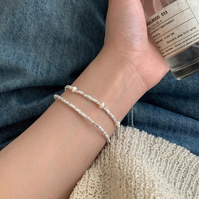 Close-up of a wrist wearing a pearl bracelet with denim fabric in the background