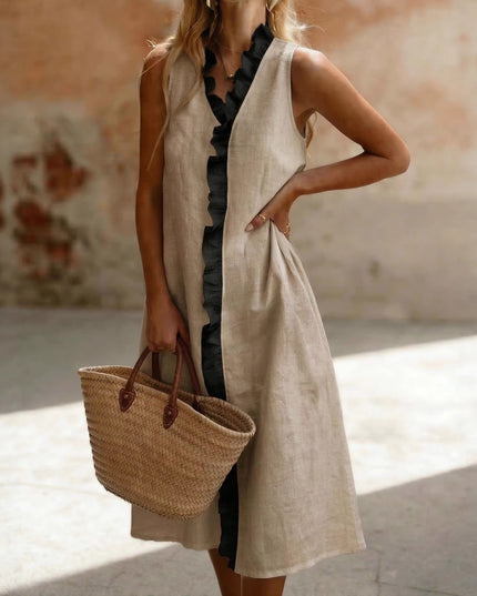 Woman in a long beige  dress holding a straw bag against a textured wall.