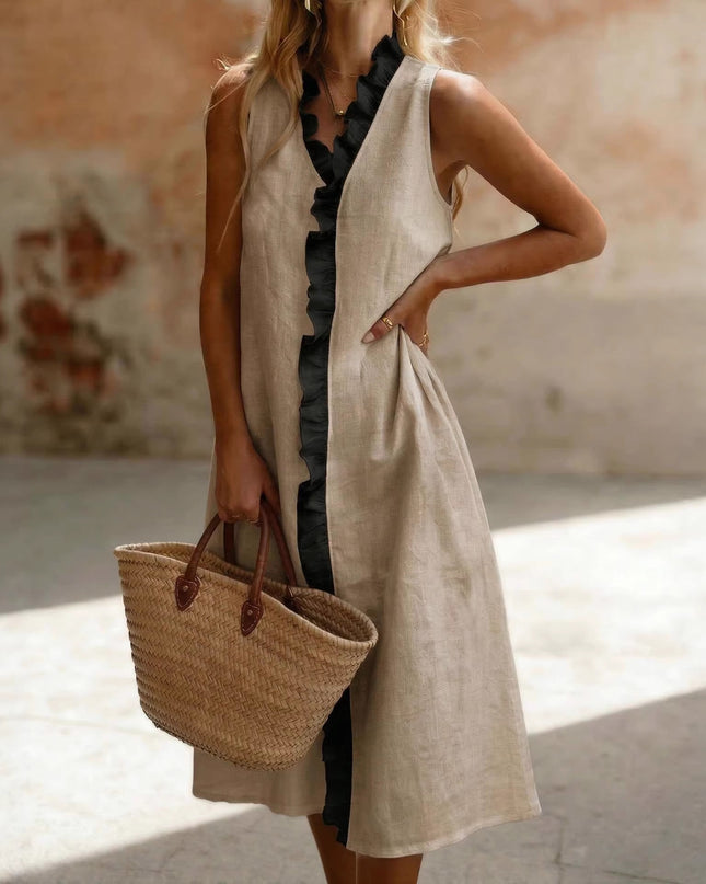 Woman in a long beige  dress holding a straw bag against a textured wall.
