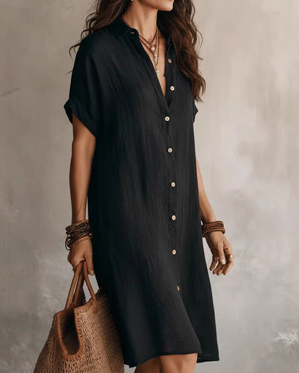 Woman wearing a black dress with buttons, holding a woven bag against a neutral background
