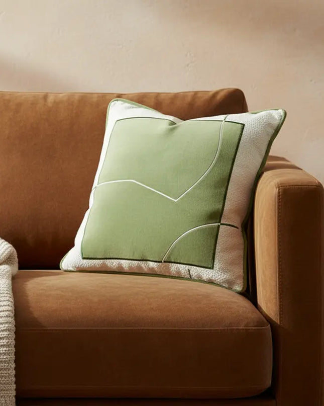 Brown sofa with a green pillow and a blanket, next to a small wooden table with a mug and book.