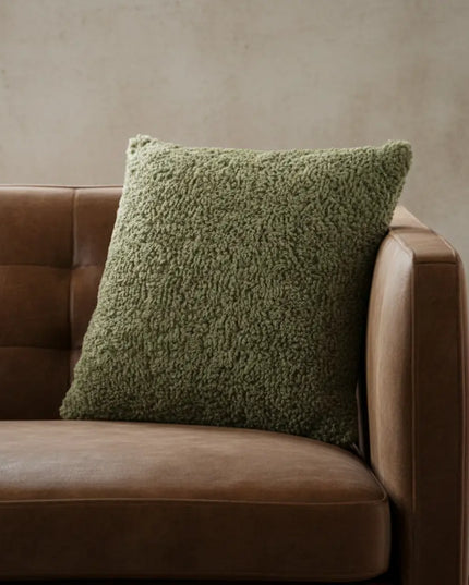 Green textured pillow on a brown leather sofa against a beige wall.