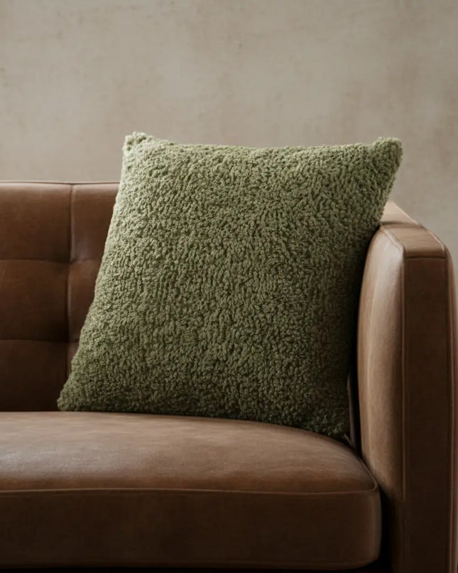 Green textured pillow on a brown leather sofa against a beige wall.