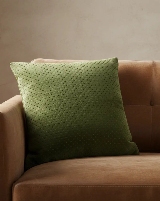 Green pillow on a brown sofa against a beige wall