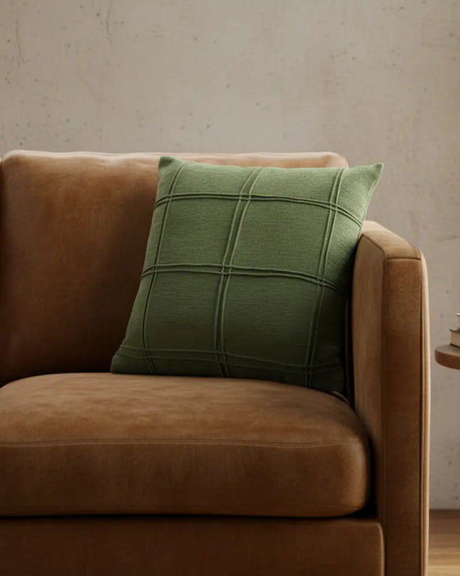 Brown sofa with a green pillow against a beige wall