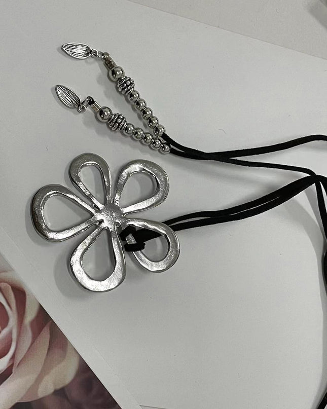 Metal flower-shaped pendant on a black cord against a white background with a floral image.