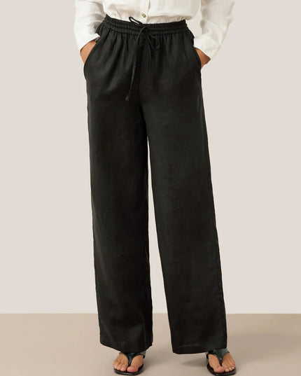 Person wearing black wide-leg pants with a white shirt on a plain background