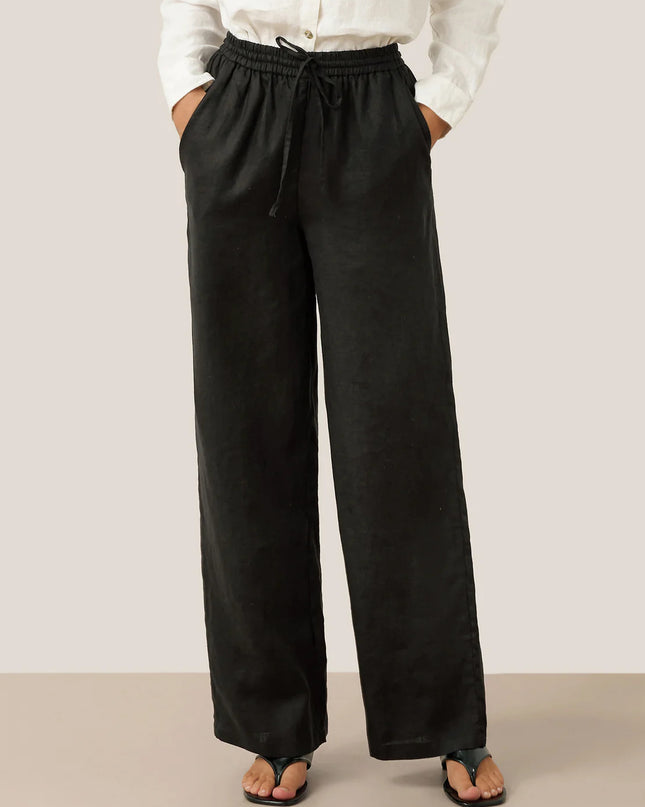 Person wearing black wide-leg pants with a white shirt on a plain background