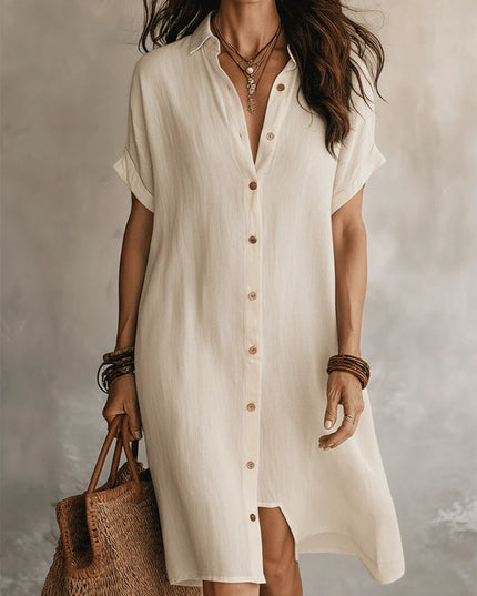 Woman wearing a white button-up dress holding a woven bag against a neutral background