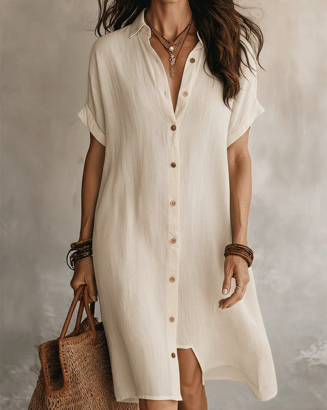 Woman wearing a white button-up dress holding a woven bag against a neutral background