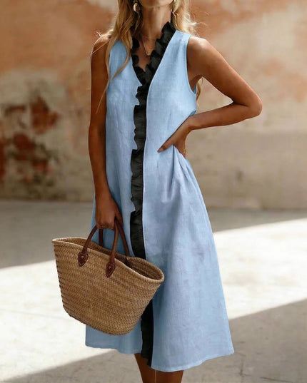 Woman wearing a light blue sleeveless dress holding a straw bag in an outdoor setting.