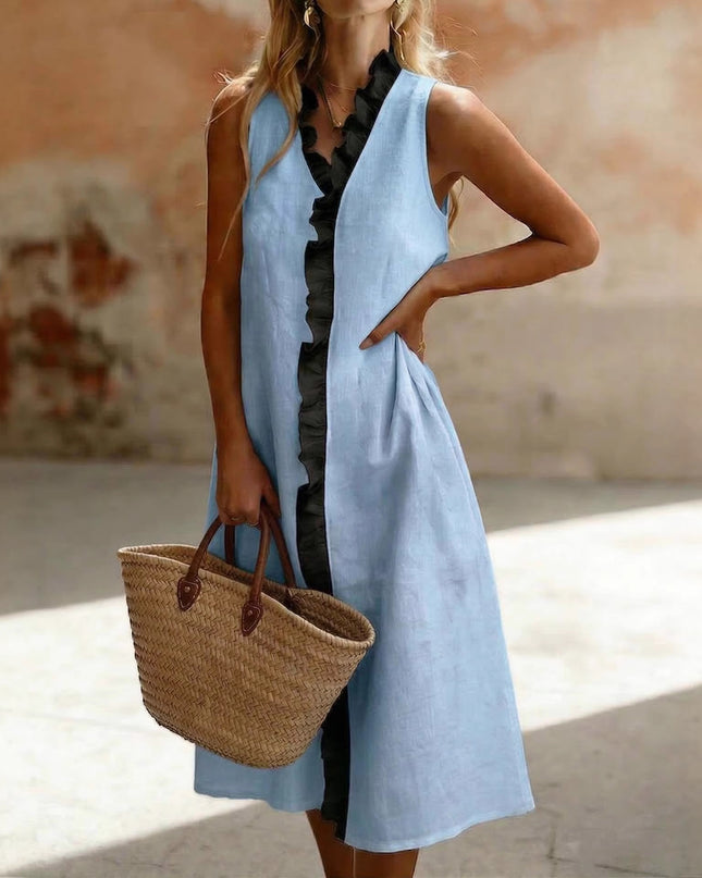 Woman wearing a light blue sleeveless dress holding a straw bag in an outdoor setting.