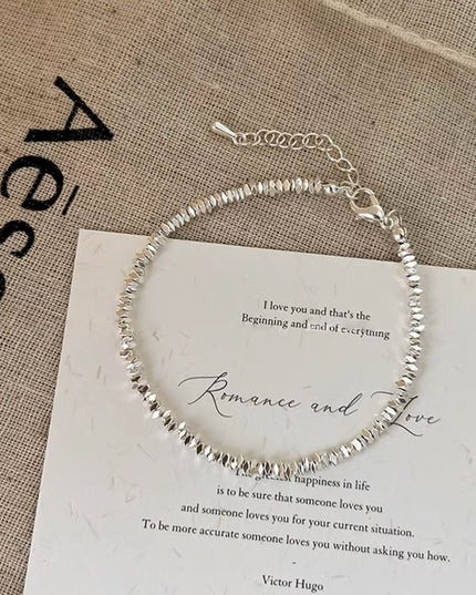 Silver beaded bracelet on a piece of paper with text