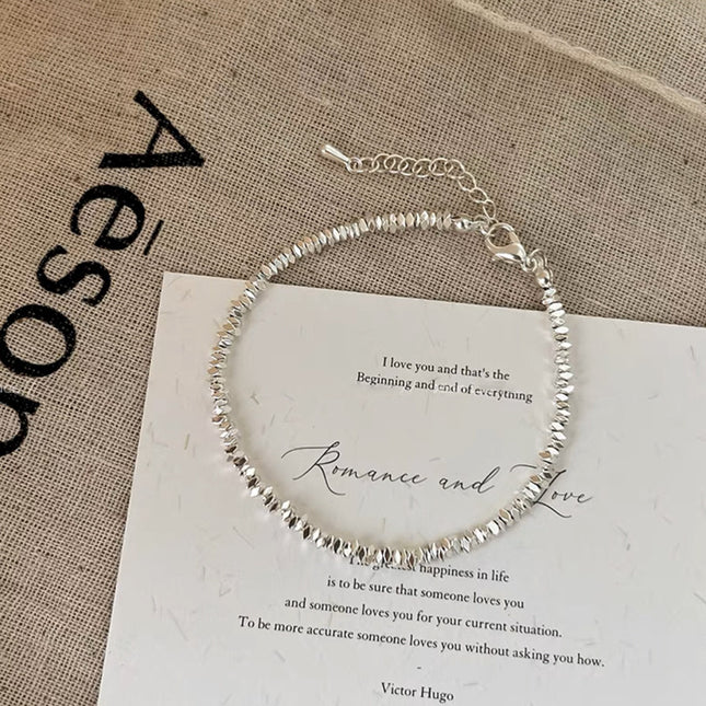 Silver beaded bracelet on a piece of paper with text