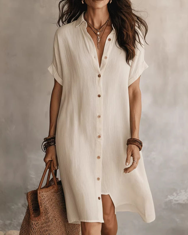 Woman wearing a beige button-up dress holding a woven bag against a neutral background