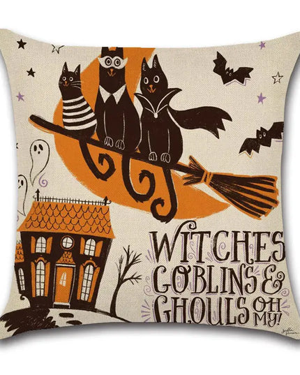 A square decorative throw pillow with a Halloween-themed illustration on a cream linen-textured background. The design features three black cats, two owls, a broomstick, a haunted house, ghosts, bats, stars, and the text 'WITCHES GOBLINS & GHOULS OH MY'.