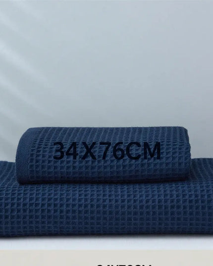 Two navy blue textured towels stacked on a white surface with dimensions '34x76cm' displayed.
