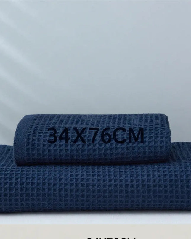 Two navy blue textured towels stacked on a white surface with dimensions '34x76cm' displayed.