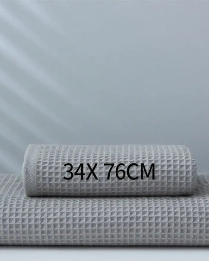 Two gray waffle-textured towels stacked on a white surface with measurement text '34X76CM' against a light gray background.