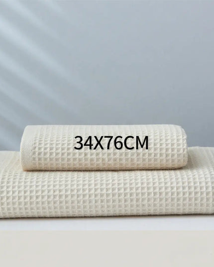 Two folded beige towels on a light gray background with text indicating size 34x76cm.