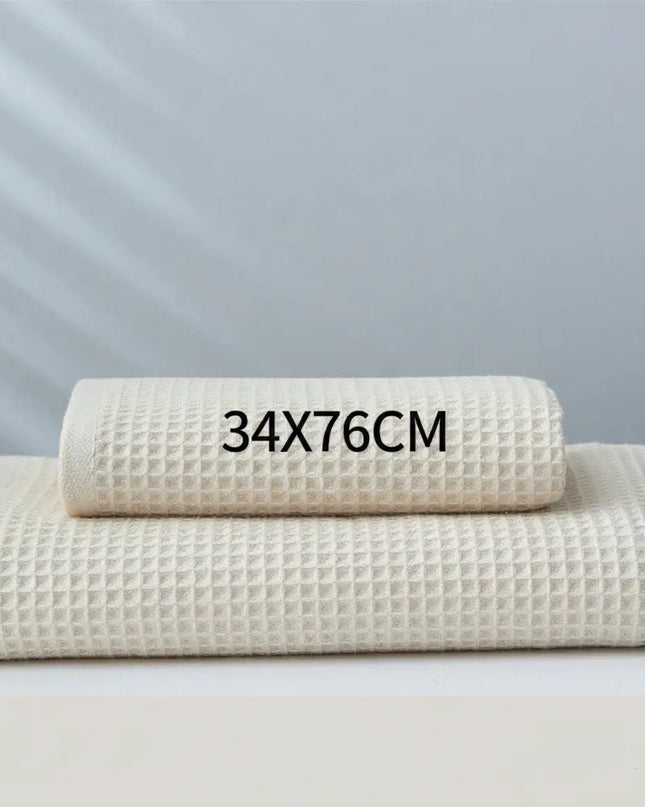 Two folded beige towels on a light gray background with text indicating size 34x76cm.