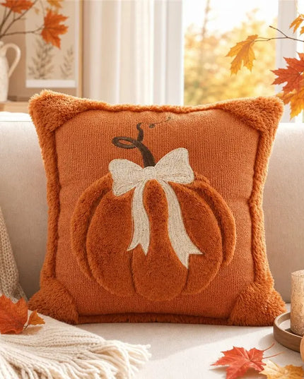 Decorative pillow with pumpkin and bow design on a couch with autumn leaves and decor.