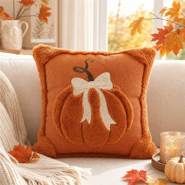 Decorative pillow with pumpkin and bow design on a couch with autumn leaves and decor.