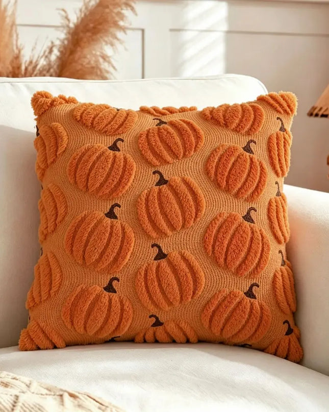 An orange textured throw pillow with a 3D pumpkin pattern and small dark brown stems, resting on a white armchair in a cozy living room setting.