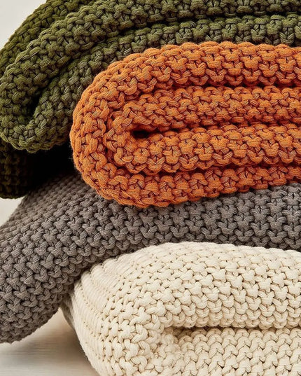 Pile of 4 throw knitted blankets in green, orange, gray and milk colors