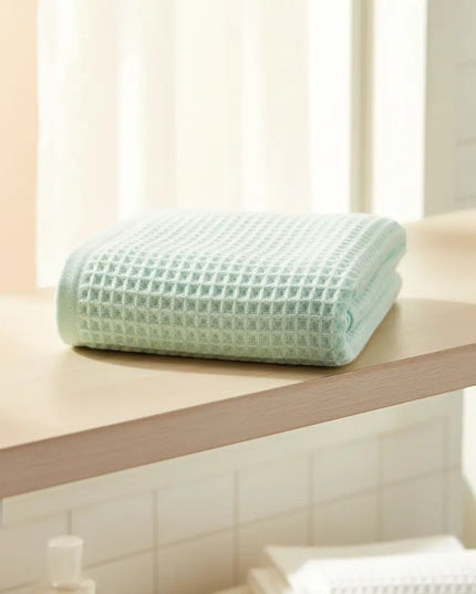 Folded light green blanket on a wooden surface with a blurred indoor background