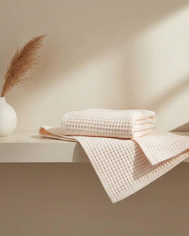 Folded towels on a shelf with a vase and decorative plant against a neutral wall.
