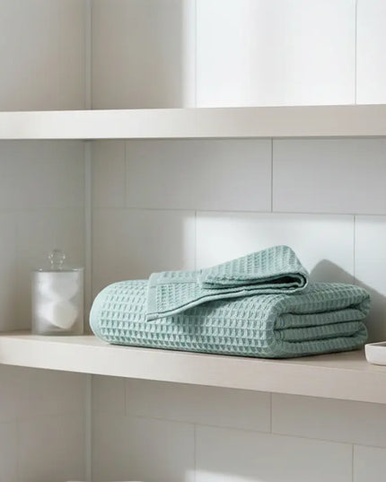 Folded light blue towel on a white shelf in a bathroom setting
