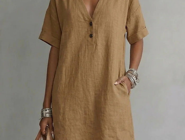 Woman wearing a brown dress holding a matching bag against a neutral background