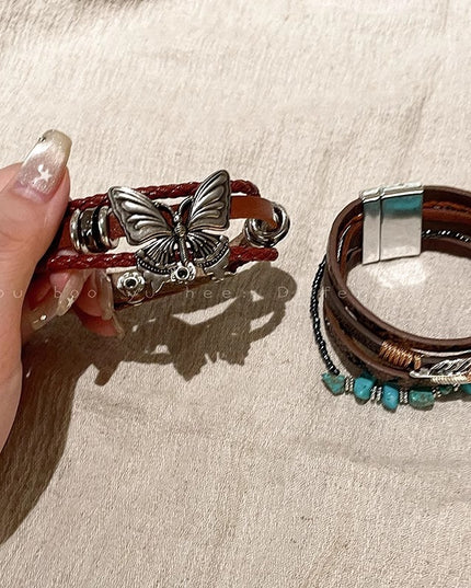 Two leather bracelets with butterfly and turquoise stone designs on a beige surface.