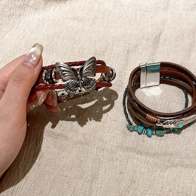 Two leather bracelets with butterfly and turquoise stone designs on a beige surface.