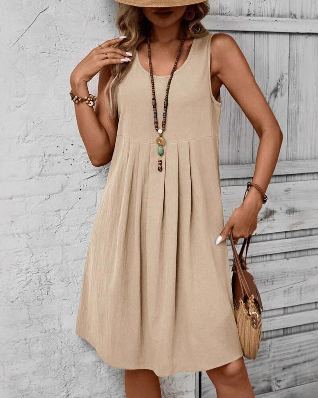 Woman wearing a beige sleeveless dress against a textured wall.