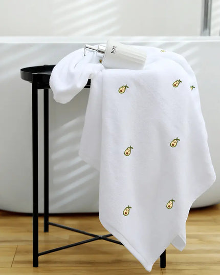 White towel with embroidered designs on a black stool next to a white bathtub.