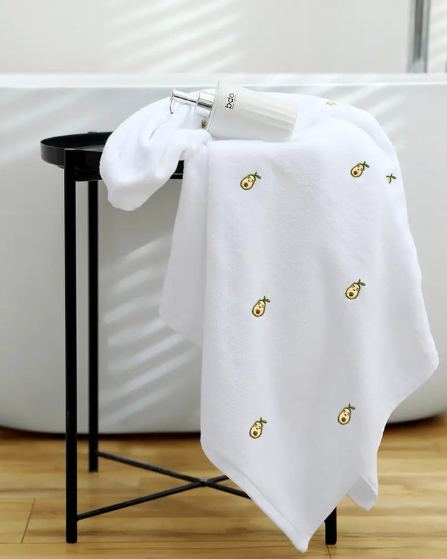 White towel with embroidered designs on a black stool next to a white bathtub.