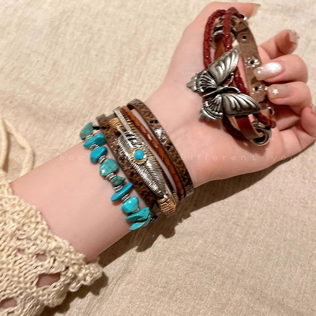 Hand wearing multiple bracelets with a butterfly charm on a beige background